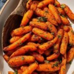 Golden brown and caramelized air fryer baby carrots seasoned with herbs in a black air fryer basket.