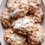 A stack of golden brown oatmeal cookies filled with diced apples and cinnamon on a wire cooling rack.