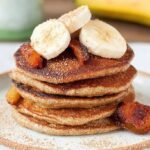 Stack of golden brown banana oat pancakes topped with fresh fruit on a white plate.