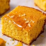 A square of golden almond flour cornbread sitting on a wooden board next to a bowl of chili.