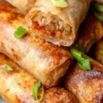 Golden brown and crispy spring rolls stacked on a plate with dipping sauce.