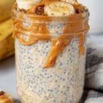 A glass jar filled with creamy peanut butter banana overnight oats topped with fresh fruit