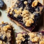 A close up of healthy blueberry crumble bars with a golden oat topping and jammy purple filling