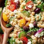 A colorful Greek Chickpea Pasta Salad with tomatoes, cucumbers, and feta cheese in a large glass bowl.