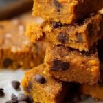 A stack of fudgy sweet potato blondies with melted chocolate chips on a parchment-lined tray