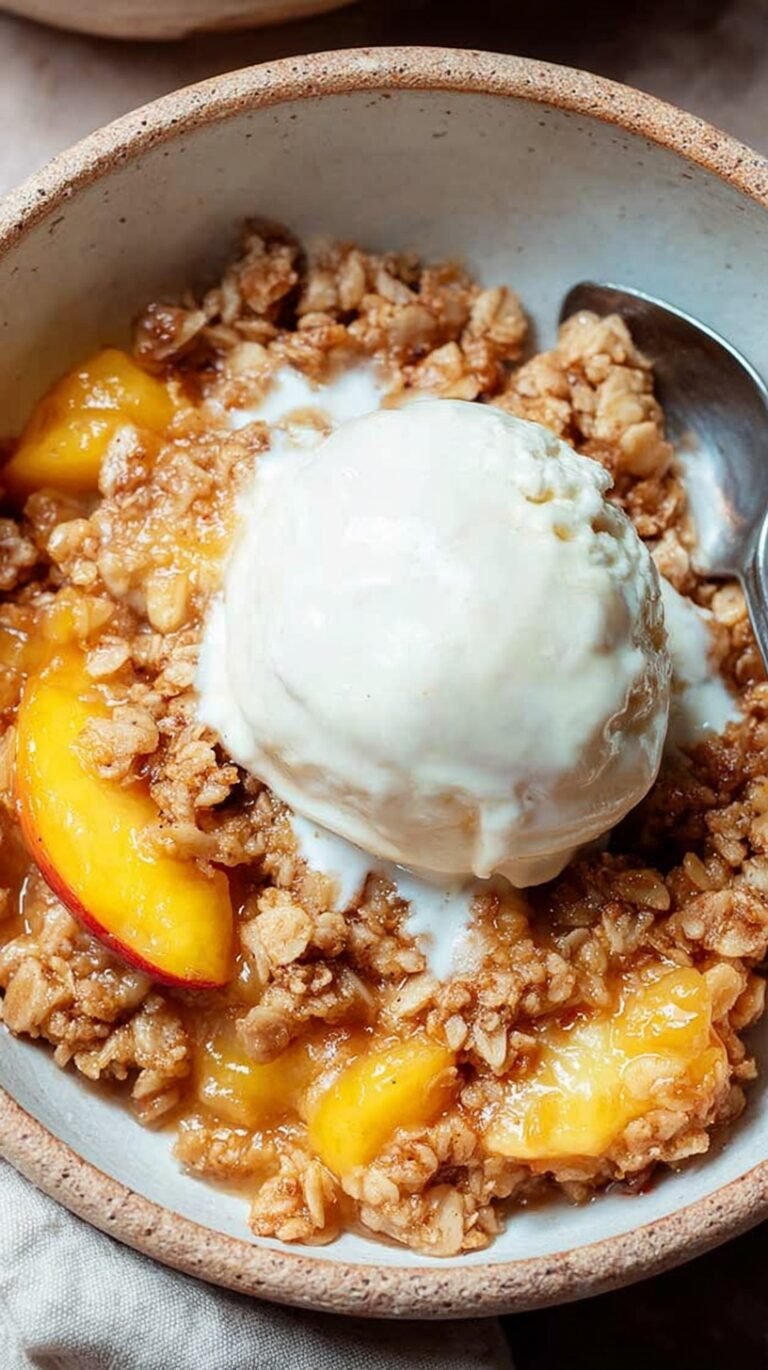 A golden brown healthy peach crisp in a glass baking dish with fresh peach slices and a crunchy oat topping.