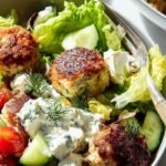 Golden brown baked chicken meatballs with feta cheese and fresh herbs on a baking sheet