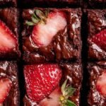 A stack of pink strawberry brownies drizzled with white sugar glaze on a white plate.
