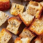 Golden brown sourdough bread croutons on a baking sheet with herbs