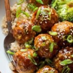 A plate of glazed golden brown turkey meatballs topped with green onions and sesame seeds over white rice.