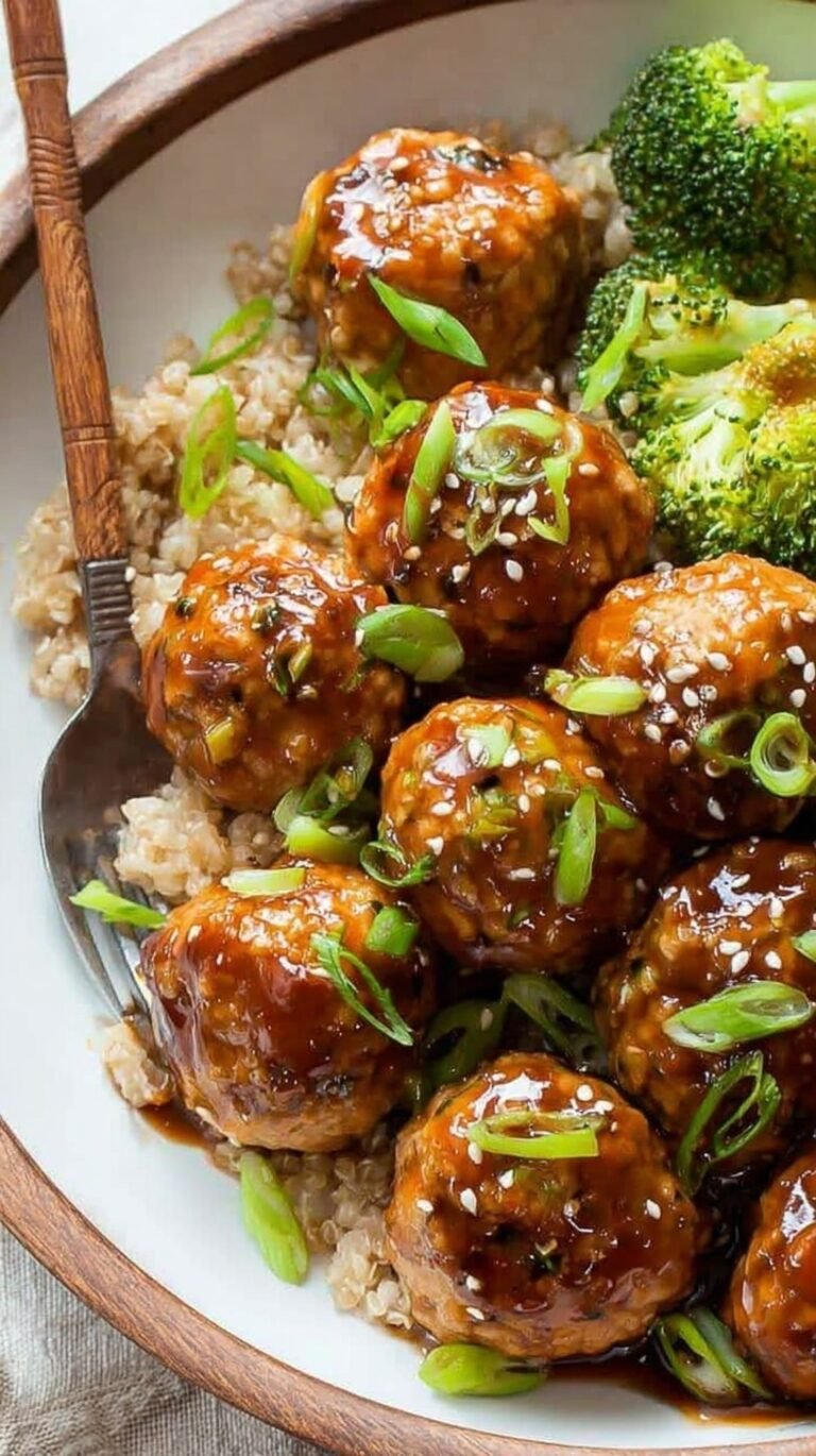 A plate of glazed golden brown turkey meatballs topped with green onions and sesame seeds over white rice.