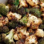 Golden brown roasted broccoli and cauliflower florets in an air fryer basket with lemon wedges