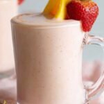 A bright pink and orange fruit smoothie in two glasses with fresh strawberry garnishes.