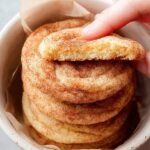A pile of soft, golden snickerdoodle cookies coated in cinnamon sugar on a wire cooling rack.