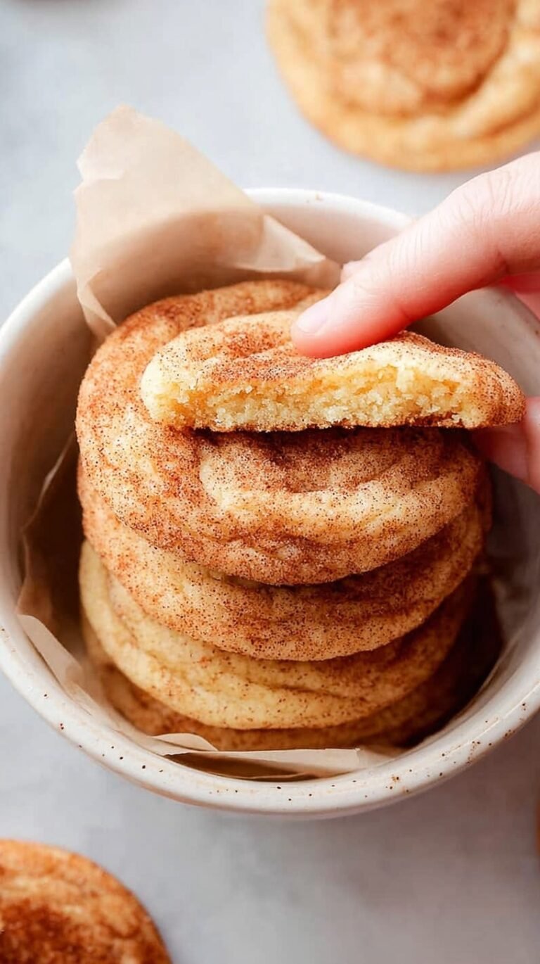 A pile of soft, golden snickerdoodle cookies coated in cinnamon sugar on a wire cooling rack.