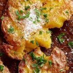 Golden brown crispy smashed fingerling potatoes seasoned with rosemary and garlic on a parchment-lined baking sheet.