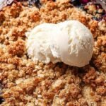 A golden brown apple and blueberry crumble in a white ceramic baking dish with bubbling fruit juices