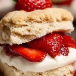 A stack of gluten-free strawberry shortcakes with fresh whipped cream and sliced berries on a white plate