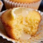 A tray of golden lemon drizzle cupcakes with a sparkling sugar glaze and fresh lemon zest on top.
