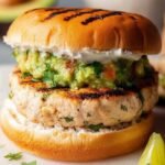 A golden-brown cilantro lime chicken burger on a toasted brioche bun with avocado and red onion.