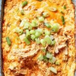 A warm dish of healthy buffalo chicken dip topped with melted cheese and green onions.