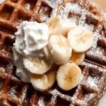 Golden brown flourless banana oat waffles topped with fresh berries on a white plate