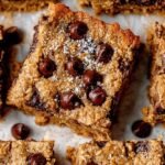 A stack of golden brown oatmeal bars with dark chocolate chips on a wooden board.
