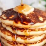 A stack of golden brown fluffy oat milk pancakes topped with maple syrup and fresh berries.