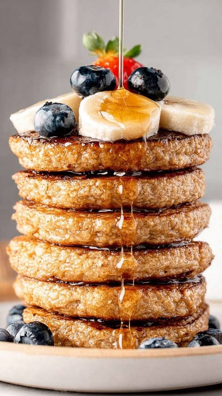 A stack of golden brown protein oatmeal blender pancakes topped with fresh banana slices and maple syrup.