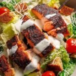 A fresh Caesar salad topped with a blackened salmon fillet and shaved parmesan cheese.