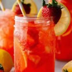 A refreshing highball glass of Strawberry Lemonade Vodka garnished with a lemon wheel on a sunny table.