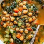 A bowl of creamy yellow chickpea soup garnished with fresh parsley and lemon slices.