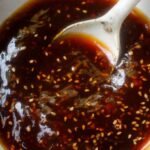 A jar of glossy, dark brown homemade teriyaki sauce with fresh ginger and garlic nearby.