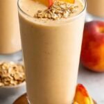 A tall glass of creamy yellow banana peach protein smoothie with a straw