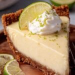 A slice of creamy gluten-free key lime pie with whipped cream and lime zest on a white plate.