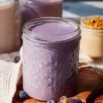 A vibrant purple blueberry banana protein smoothie in a glass with a straw
