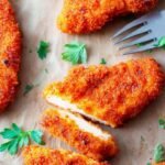 Golden brown fried chicken tenders coated in a red spicy oil glaze on a white plate.
