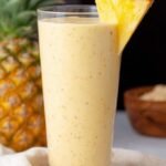 A creamy yellow mango pineapple smoothie in a tall glass with a straw