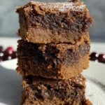 A stack of square gingerbread blondies with chocolate chips on a wooden board.