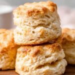 A stack of golden brown fluffy almond milk biscuits on a parchment-lined baking sheet.