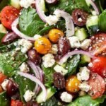 A fresh bowl of Greek spinach salad with feta cheese, olives, and cucumbers