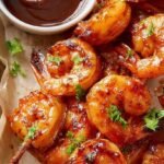 Skewers of grilled BBQ shrimp with a charred glaze on a grill grate.