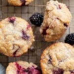 A close up of golden brown gluten free blackberry muffins with fresh berries