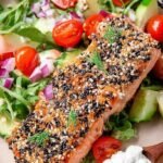 A baked salmon fillet topped with everything bagel seasoning and served with lemon wedges.