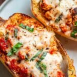 Two halves of roasted spaghetti squash filled with chicken parmesan and melted mozzarella cheese