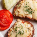 A toasted open face tuna melt with bubbling melted cheddar cheese and fresh parsley on a baking sheet.