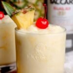 A chilled glass of Skinny Bacardi Pina Colada garnished with a fresh pineapple wedge on a sunny table.