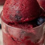 A scoop of vibrant purple blueberry peach sorbet in a glass bowl with fresh fruit garnish