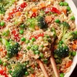 A bowl of vibrant brown rice fried with eggs, peas, carrots, and green onions in a dark skillet.