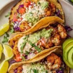 Roasted cauliflower tacos topped with red cabbage and cilantro yogurt crema on a plate with lime wedges